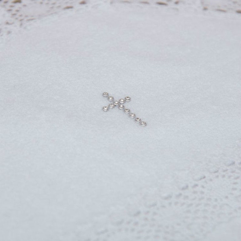 May include: A white fabric with a small silver cross made of rhinestones.