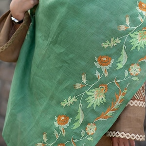 May include: A green shawl with embroidered floral designs in shades of orange, white, and green.