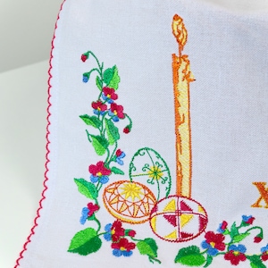 Pode incluir: Tecido branco bordado com uma borda festonada vermelha. O design apresenta uma vela, tr&ecirc;s ovos de P&aacute;scoa e uma videira com folhas verdes e flores rosa e azuis.