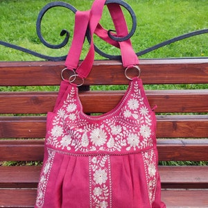 Peut inclure: Un sac cabas en tissu rose avec des motifs floraux brod&eacute;s blancs. Le sac a deux anses et un fond pliss&eacute;.
