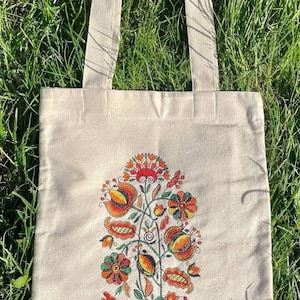 May include: A white canvas tote bag with a floral design embroidered on the front. The flowers are orange, red, yellow, and green.