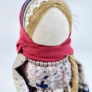 May include: A handmade rag doll with a red scarf, a white lace trim, and a pearl necklace. The doll has long, brown hair and a white fabric face.