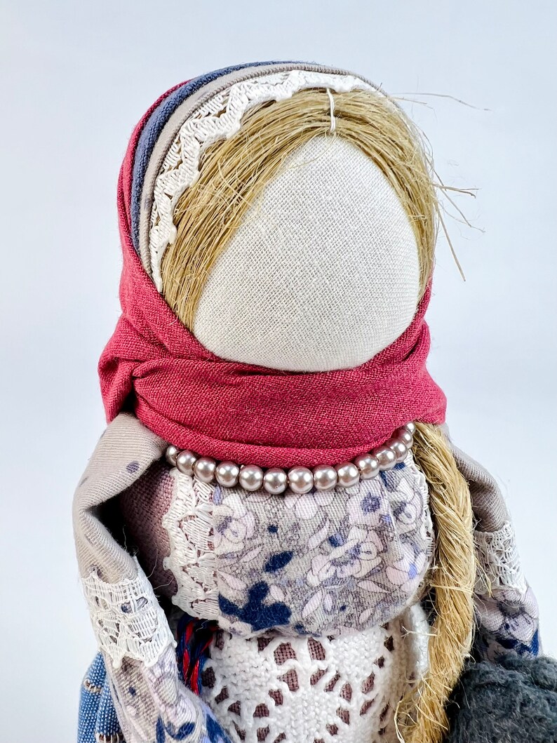 May include: A handmade rag doll with a red scarf, a white lace trim, and a pearl necklace. The doll has long, brown hair and a white fabric face.