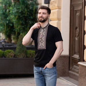 Peut inclure: Un homme portant une chemise noire &agrave; manches courtes avec un motif brod&eacute; traditionnel et un jean bleu.