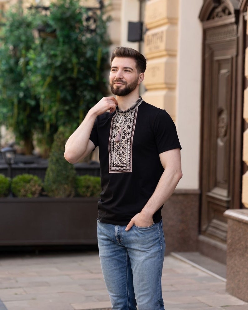 Peut inclure: Un homme portant une chemise noire &agrave; manches courtes avec un motif brod&eacute; traditionnel et un jean bleu.