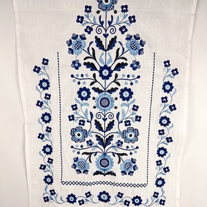 May include: White linen fabric with blue embroidered floral design. The design features a central floral motif with smaller floral motifs along the sides.