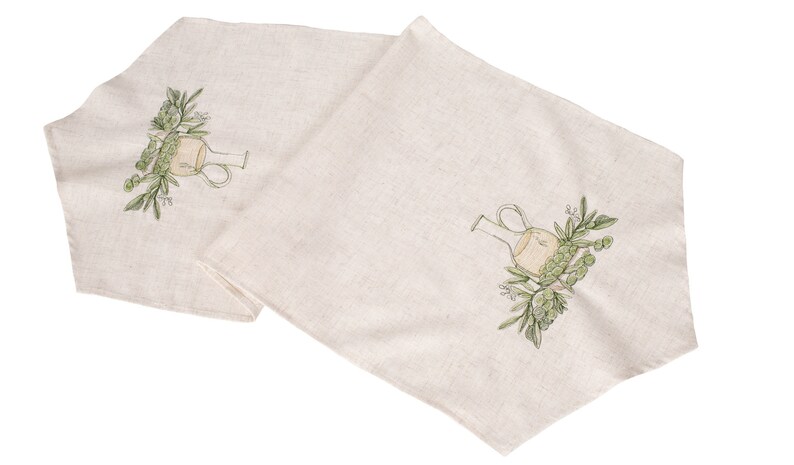 May include: Two beige linen table runners with an embroidered design of a green olive branch and a clear glass bottle.