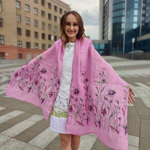 Puede incluir: Una bufanda de lino rosa con un patr&oacute;n floral. La bufanda est&aacute; drapeada sobre los hombros de una persona y ondea con el viento.