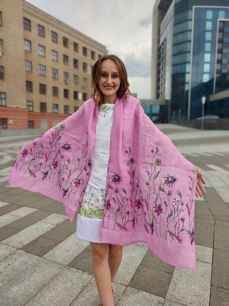 Puede incluir: Una bufanda de lino rosa con un patr&oacute;n floral. La bufanda est&aacute; drapeada sobre los hombros de una persona y ondea con el viento.