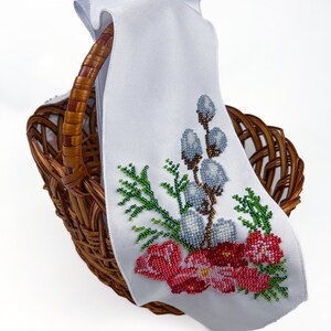 May include: A white fabric basket liner with embroidered flowers and willow branches in shades of red, green, blue, and brown. The liner is in a wicker basket.