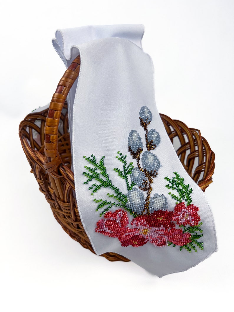 May include: A white fabric basket liner with embroidered flowers and willow branches in shades of red, green, blue, and brown. The liner is in a wicker basket.