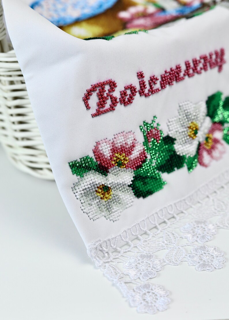 K&ouml;nnte beinhalten: Wei&szlig;es besticktes Tuch mit floralen und textlichen Details. Der Text "Bożemu" ist aus roten Perlen. Das florale Design umfasst wei&szlig;e, rosa und rote Blumen mit gr&uuml;nen Bl&auml;ttern. Der untere Rand hat eine wei&szlig;e Spitzentrimmung.