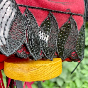 Puede incluir: Un sombrero de tela roja con ribete de encaje negro y lentejuelas. El sombrero est&aacute; sobre una base de madera.