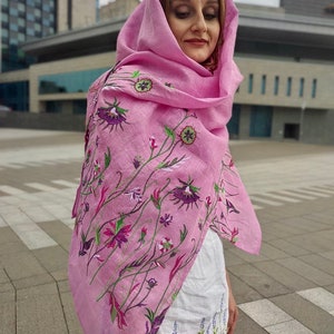 Puede incluir: Una bufanda de lino rosa con bordado floral. La bufanda est&aacute; drapeada sobre los hombros y la cabeza de una persona. El bordado es en tonos de morado, verde y blanco.