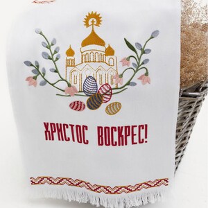 Op de afbeelding: Witte geborduurde keukendoek met een gouden kerk, bloemen en kleurrijke paaseieren. De tekst "ХРИСТОС ВОСКРЕС!" is geborduurd in rood.