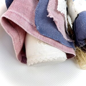 May include: A handmade rag doll with a pink, blue, and white fabric dress. The doll has a white fabric face with embroidered details.