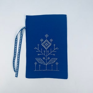 K&ouml;nnte beinhalten: Eine blaue Stofftasche mit einem wei&szlig;en gestickten Design einer stilisierten Blume. Die Tasche hat einen wei&szlig;en und blauen Kordelzug.