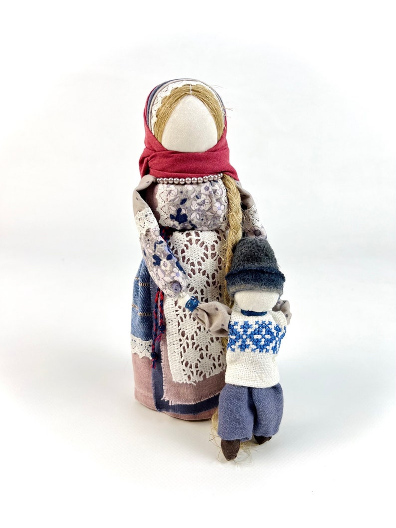 May include: A handmade fabric doll with a red headscarf and a floral dress holding a smaller fabric doll wearing a blue hat and sweater.