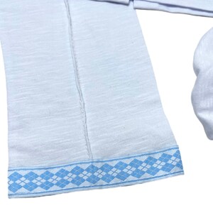 May include: White long-sleeved shirt with a blue and white patterned trim around the bottom edge.