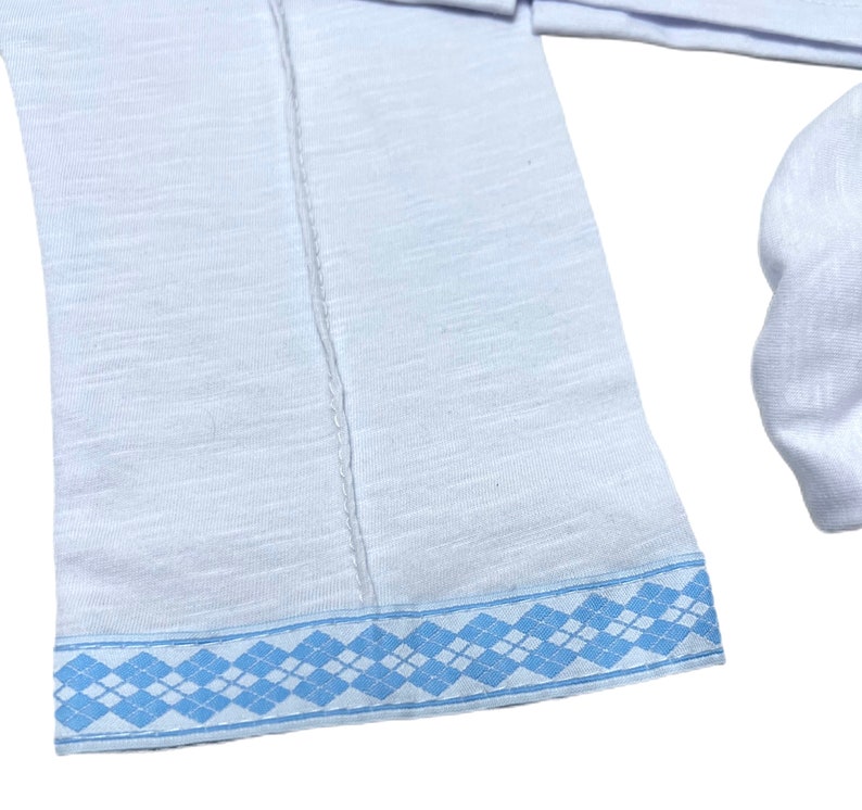 May include: White long-sleeved shirt with a blue and white patterned trim around the bottom edge.