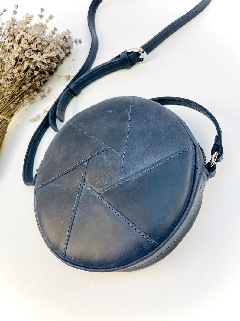 Puede incluir: Un bolso de hombro redondo de cuero azul oscuro con un dise&ntilde;o geom&eacute;trico. El bolso tiene una correa larga ajustable.