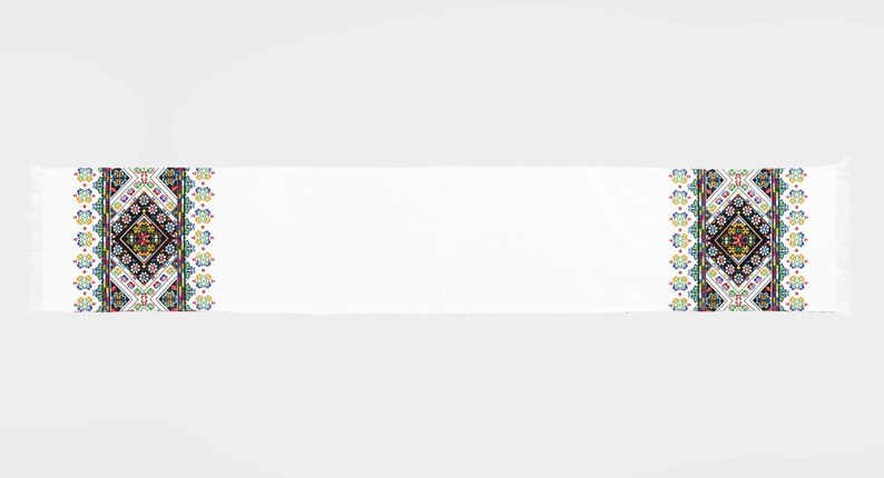 May include: White fabric scarf with a colorful embroidered design featuring geometric shapes and floral patterns. The design is repeated on both ends of the scarf.