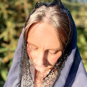 May include: A woman wearing a blue veil with black lace trim. The veil is draped over her head and shoulders.