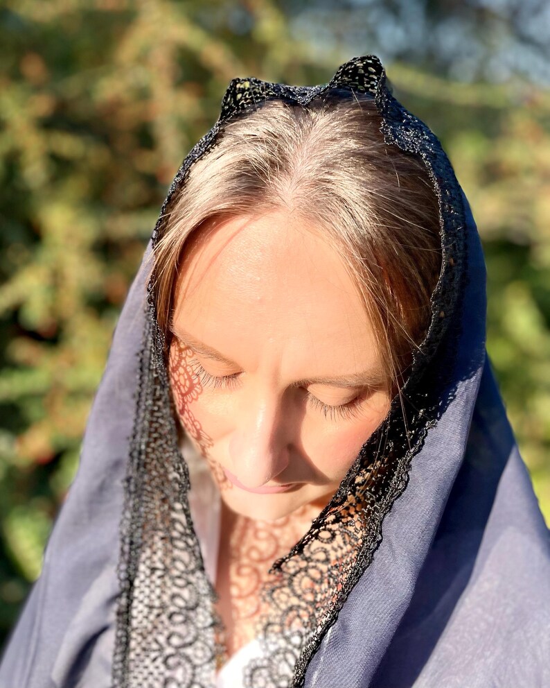 May include: A woman wearing a blue veil with black lace trim. The veil is draped over her head and shoulders.