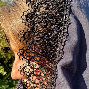 May include: A black lace veil with a scalloped edge. The veil is made of a sheer fabric and has a delicate floral pattern.