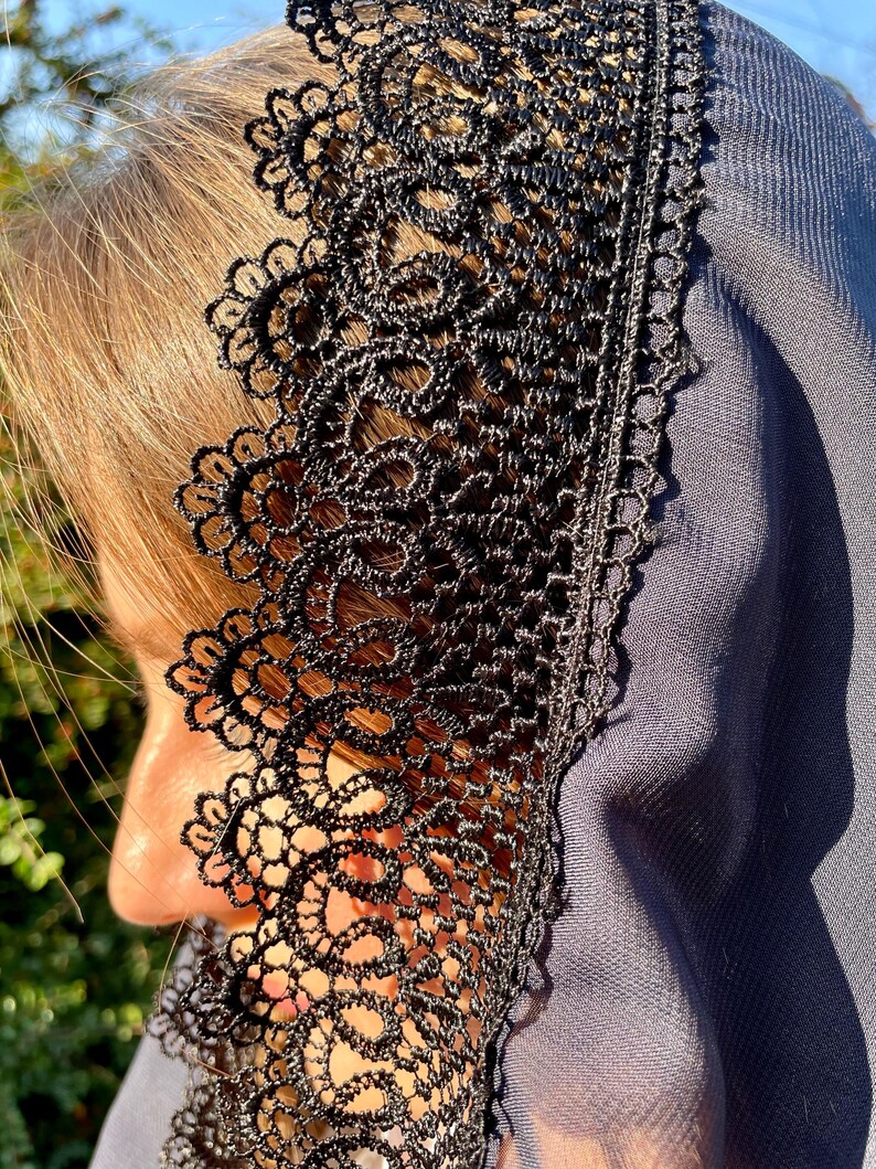 May include: A black lace veil with a scalloped edge. The veil is made of a sheer fabric and has a delicate floral pattern.