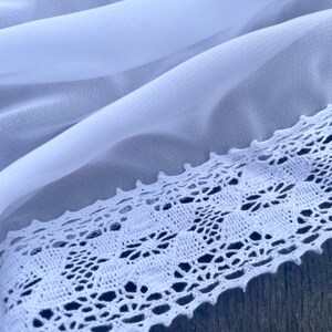 Pu&ograve; includere: Tessuto bianco trasparente con un bordo in pizzo all'uncinetto bianco. Il pizzo ha un delicato motivo floreale.