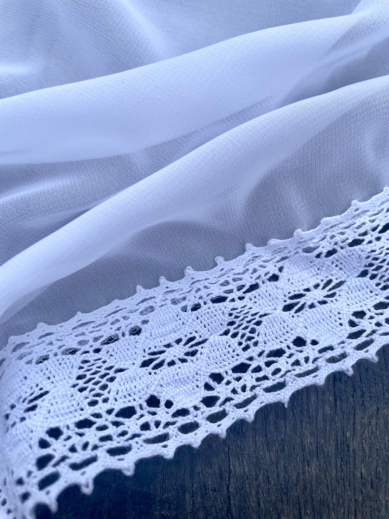 Pu&ograve; includere: Tessuto bianco trasparente con un bordo in pizzo all'uncinetto bianco. Il pizzo ha un delicato motivo floreale.