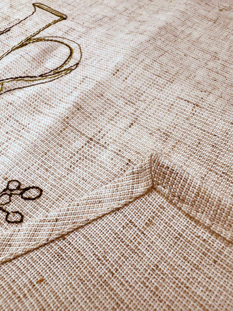 May include: Close-up of a beige linen fabric with a stitched seam. The fabric has a subtle woven texture.