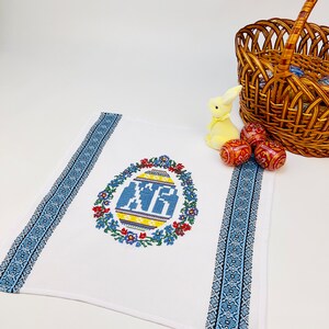 Peut inclure: Serviette de cuisine blanche brod&eacute;e avec un motif d'&oelig;uf de P&acirc;ques bleu et jaune entour&eacute; de fleurs. La serviette a des bordures bleues et blanches.