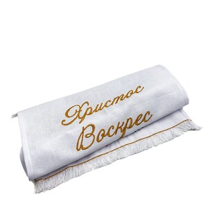 Pu&ograve; includere: Tovagliolo da t&egrave; in lino bianco con una frase ricamata in oro "Христос Воскрес" (Cristo &egrave; risorto) in scrittura cirillica. Il tovagliolo ha un bordo a frangia bianca.