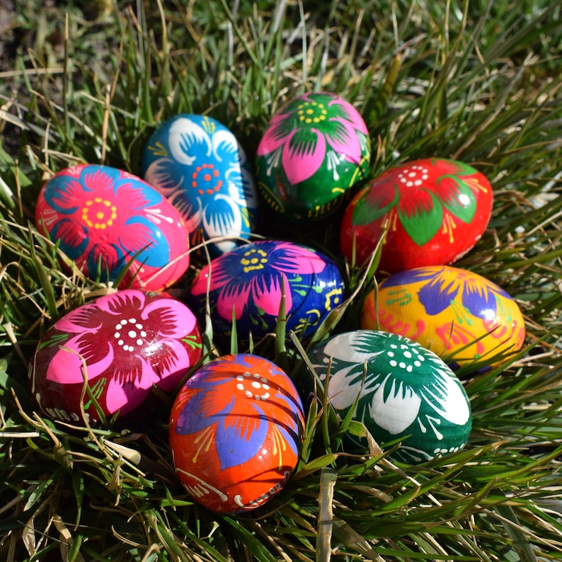 May include: A collection of vibrantly painted Easter eggs nestled in green grass. The eggs feature floral designs in various colors, including pink, blue, red, green, and orange. Each egg is uniquely decorated with intricate patterns.