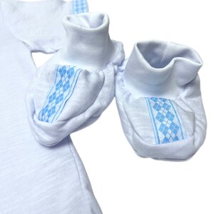 May include: A pair of white baby booties with blue and white diamond patterned trim.