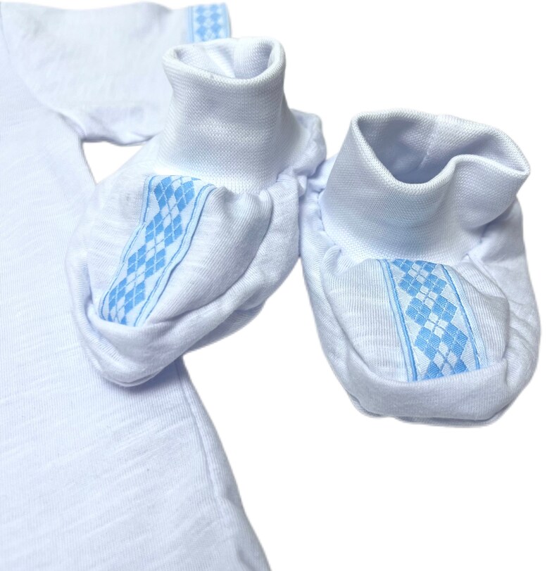 May include: A pair of white baby booties with blue and white diamond patterned trim.