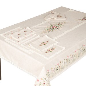 May include: A white tablecloth with embroidered floral designs and a lace trim. The tablecloth is set with four placemats and a set of pot holders.
