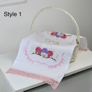 May include: White woven basket with a handle, holding a white embroidered cloth. The cloth features a floral design with pink, purple, and gold accents, and a pink lace trim. The text "Style 1" is in the upper left corner.