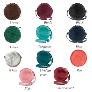 Op de afbeelding: Tien ronde leren handtassen in verschillende kleuren. Elke tas heeft een klep met een camera-sluiterontwerp. De kleuren zijn bruin, bordeaux, zwart, groen, turquoise, blauw, wit, viridiaan groen, roze en Amerikaans rood.
