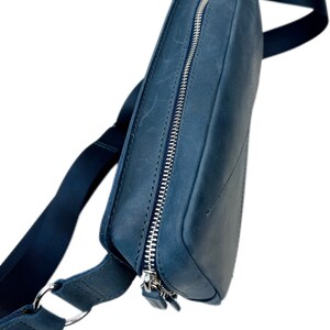 May include: A dark blue leather crossbody bag with a silver zipper and a long adjustable strap.