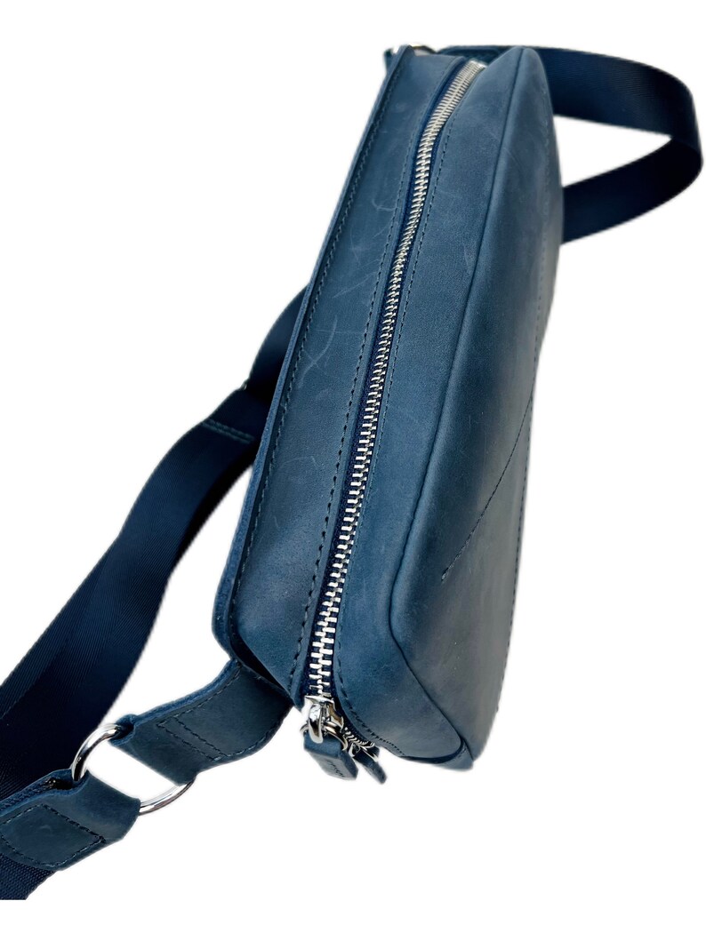 May include: A dark blue leather crossbody bag with a silver zipper and a long adjustable strap.