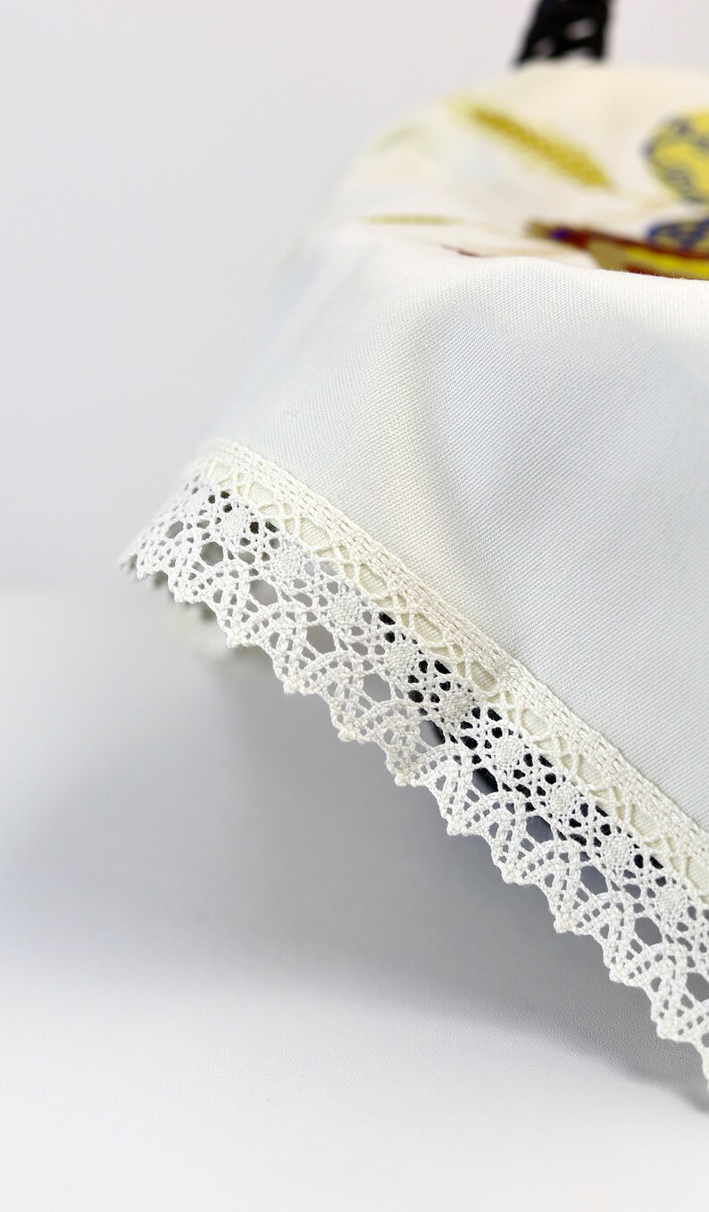 Pu&ograve; includere: Tovaglia bianca con un bordo di pizzo bianco. La tovaglia &egrave; piegata e il bordo di pizzo &egrave; visibile.