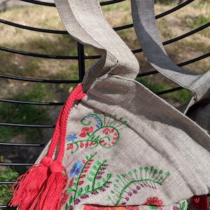 May include: A beige linen tote bag with red tassels and colorful embroidered floral designs.