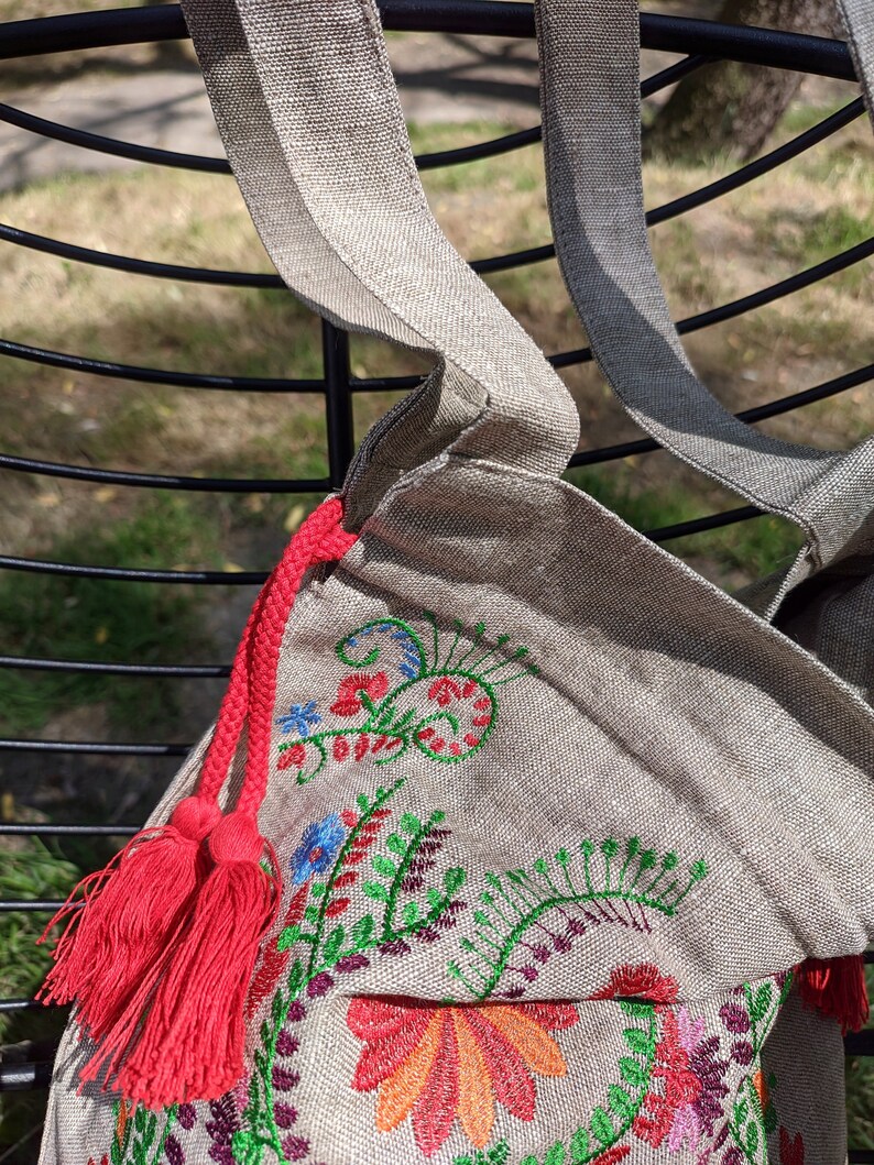 May include: A beige linen tote bag with red tassels and colorful embroidered floral designs.
