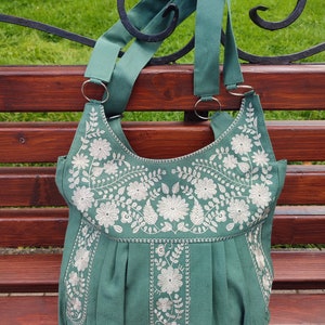 Peut inclure: Un sac cabas en toile vert sarcelle avec des motifs floraux brod&eacute;s blancs. Le sac a deux longues anses et un fond pliss&eacute;.