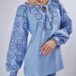 May include: A light blue embroidered blouse with a geometric pattern. The blouse has a round neckline and long sleeves.