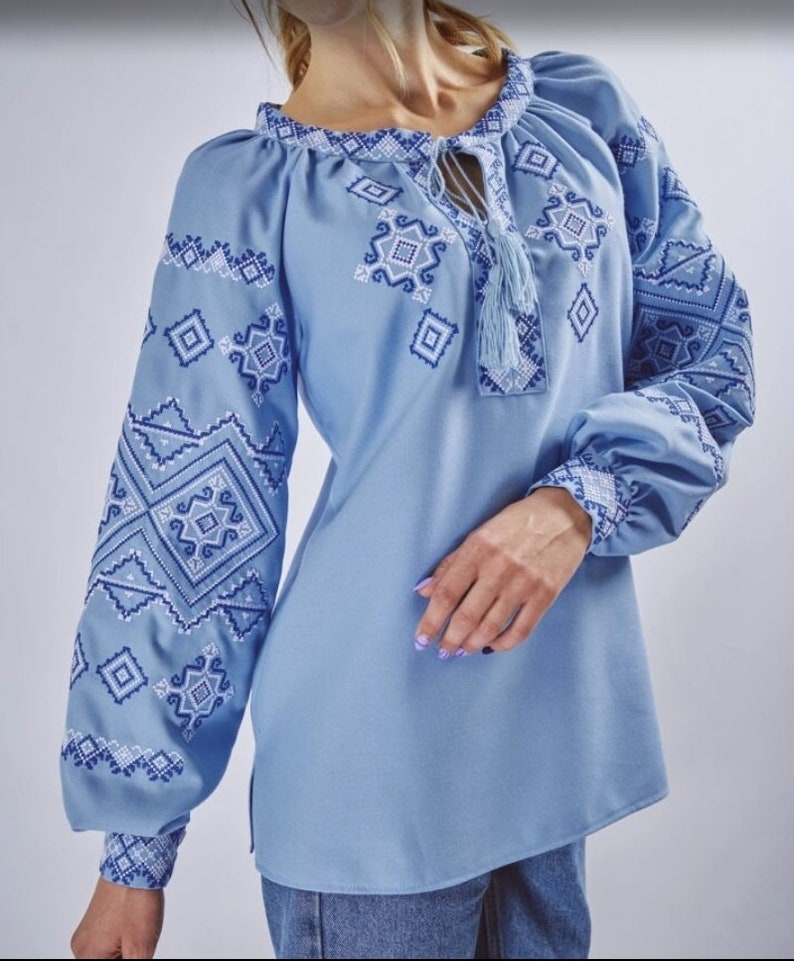 May include: A light blue embroidered blouse with a geometric pattern. The blouse has a round neckline and long sleeves.