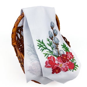 May include: White fabric with a beaded embroidery design of a floral bouquet with red, green, and white flowers and a sprig of willow branches. The fabric is folded and placed in a wicker basket.